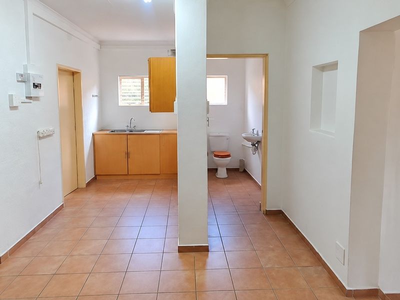 Open plan office area featuring a kitchenette with built-in cabinetry and an adjacent private restroom with standard sanitary fixtures.