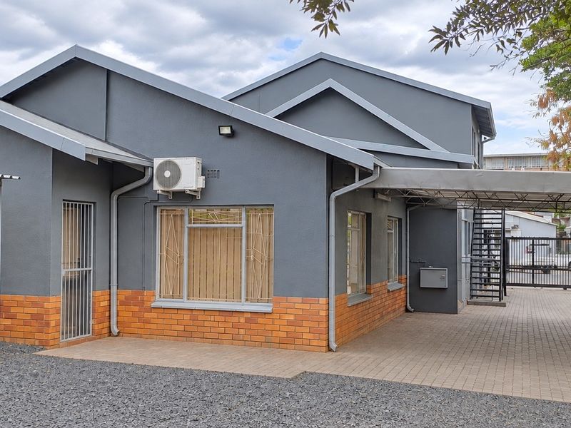 A well-maintained office building exterior featuring a brick and painted facade, covered carport, and secure gated access.