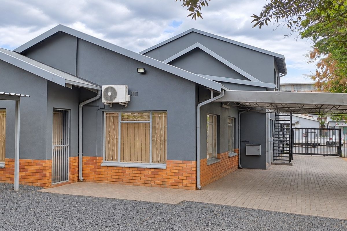 A well-maintained office building exterior featuring a brick and painted facade, covered carport, and secure gated access.
