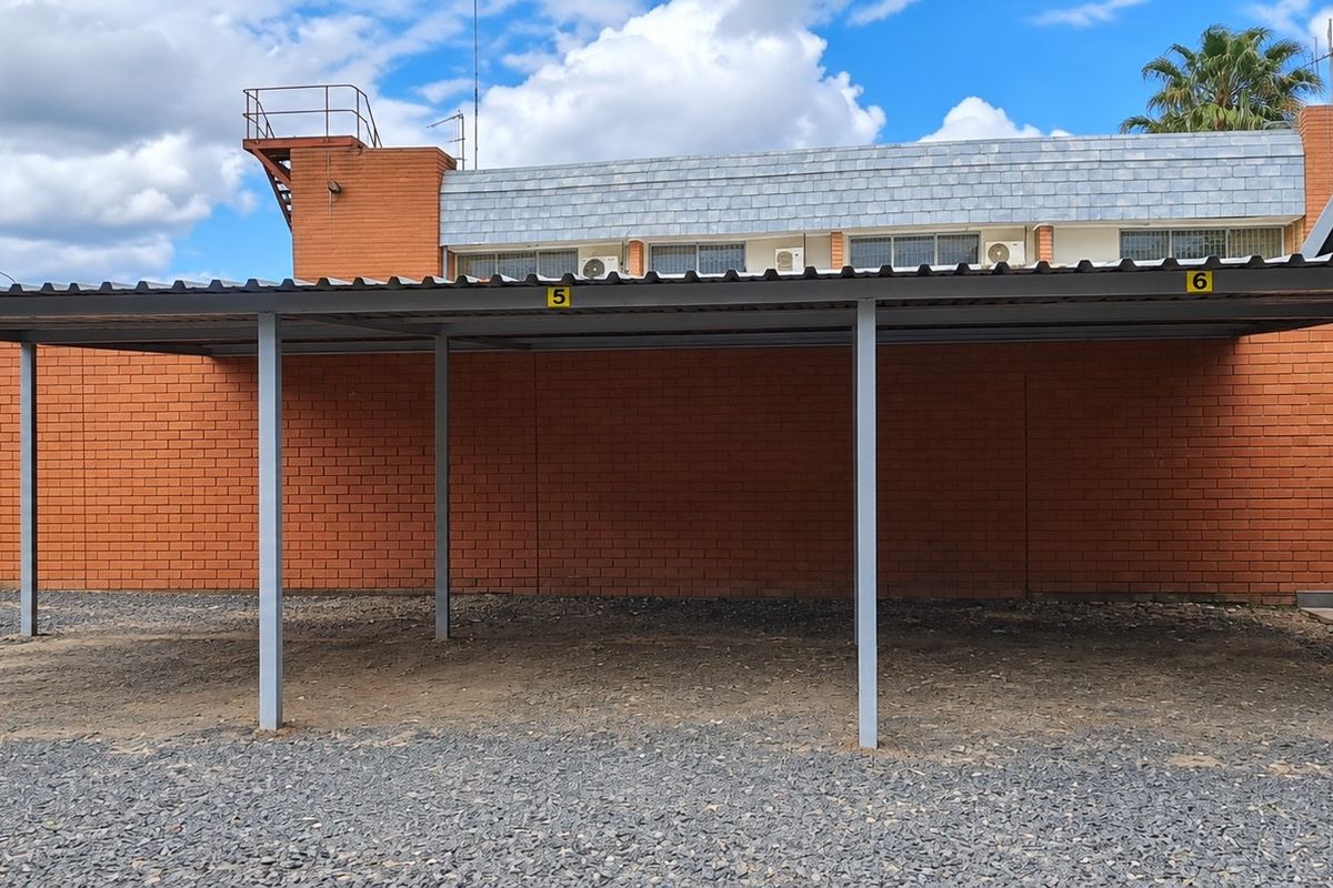 A functional outdoor carport area with numbered bays, featuring a gravel surface and brick boundary wall, suitable for office parking.