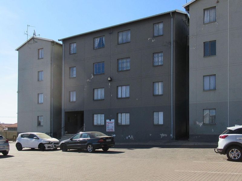 Exterior view of a multi-story apartment building featuring a paved parking area and security-enhanced windows.
