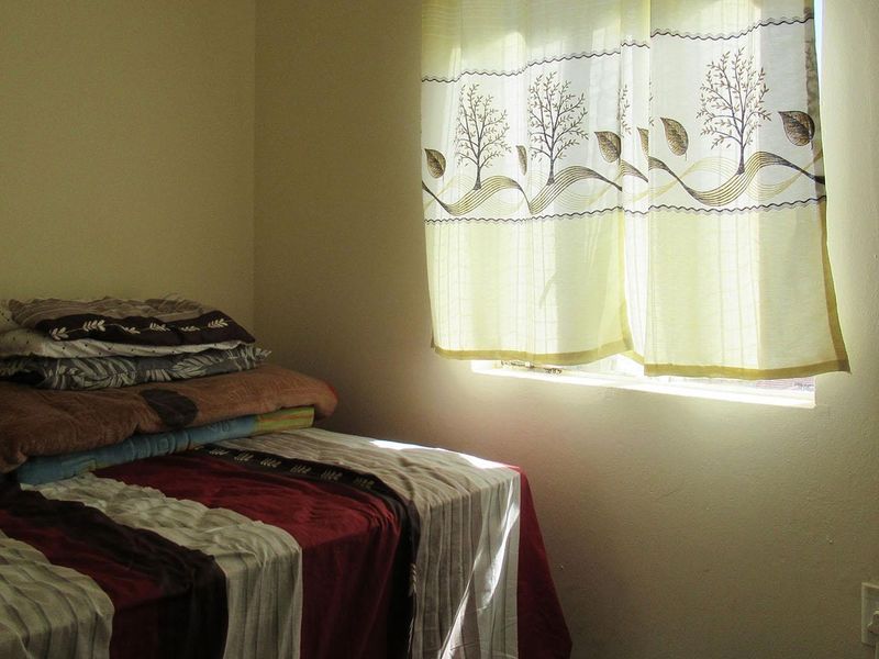 A simple bedroom featuring a window with natural light and a standard electrical outlet.