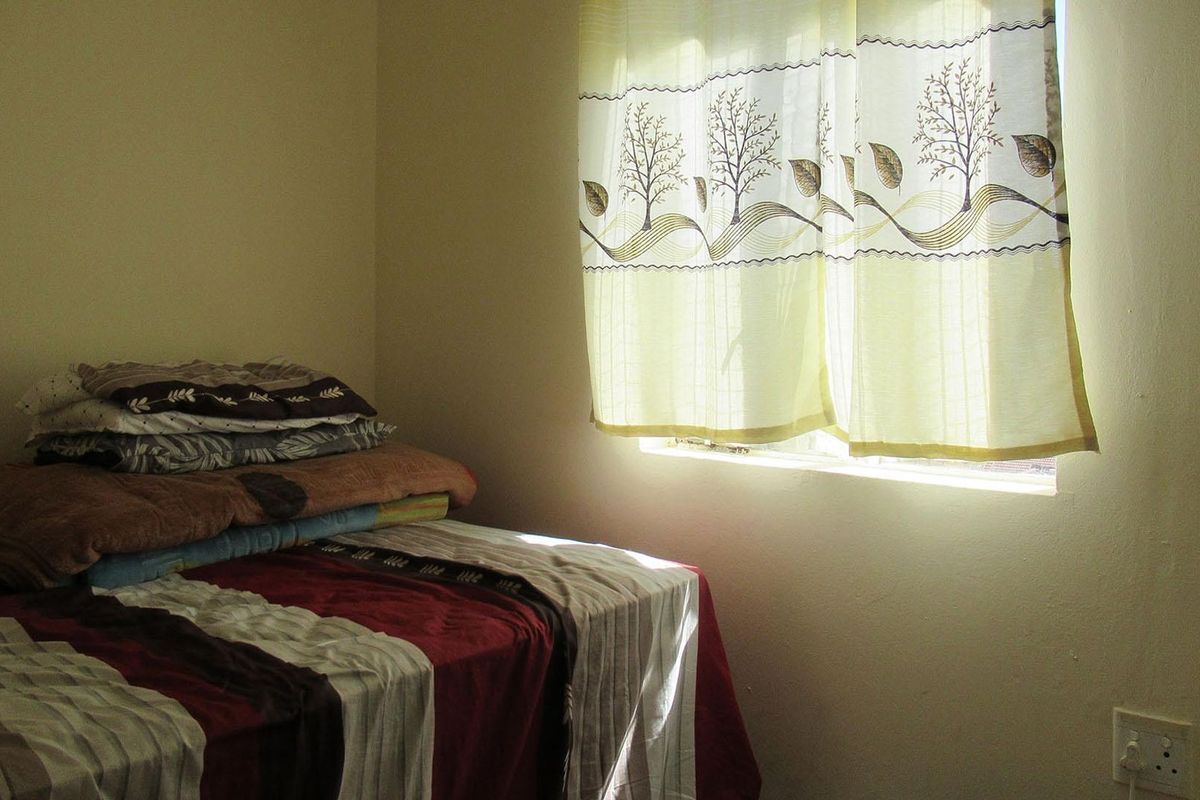A simple bedroom featuring a window with natural light and a standard electrical outlet.