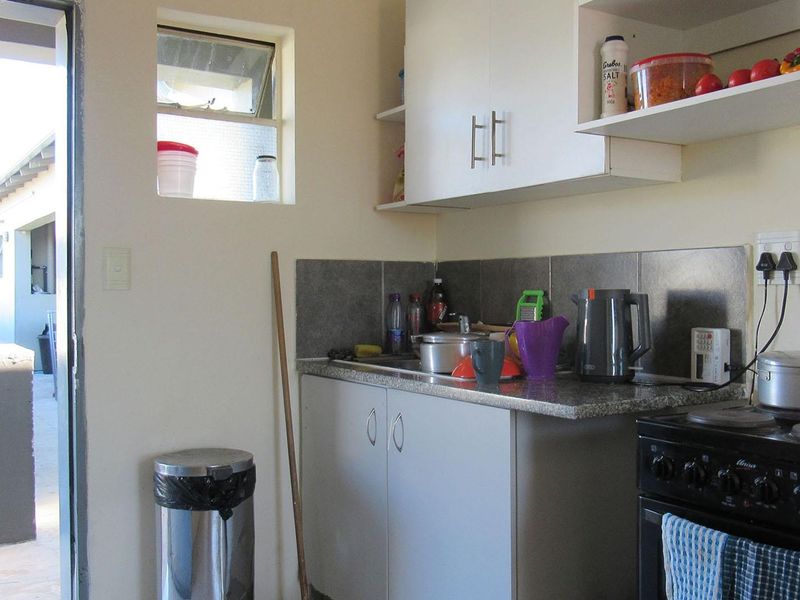 Compact kitchen featuring built-in cabinetry, stone countertops, a tiled backsplash, and a freestanding stove, with direct access to an outdoor area.
