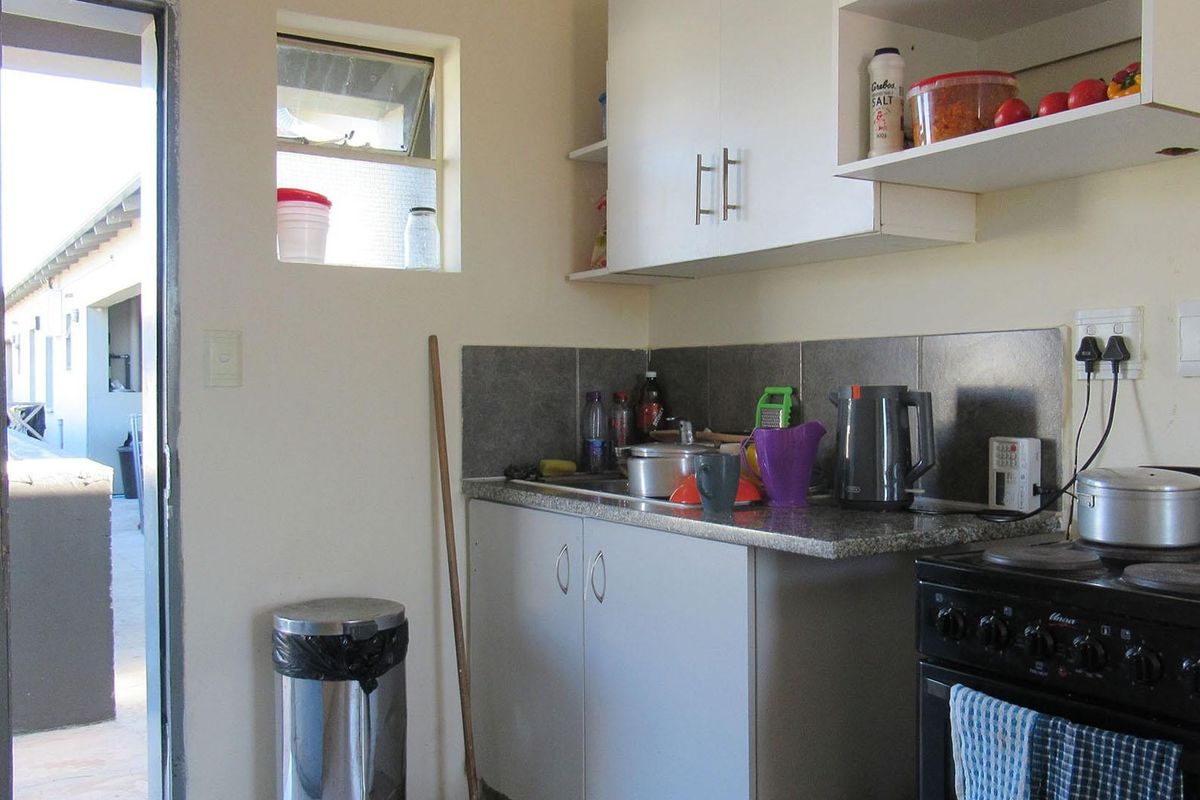Compact kitchen featuring built-in cabinetry, stone countertops, a tiled backsplash, and a freestanding stove, with direct access to an outdoor area.