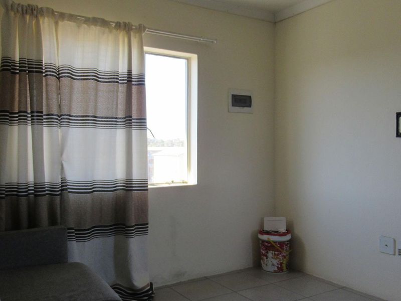 A simple living area featuring tiled flooring, a wall-mounted television bracket, and an electrical distribution board, offering a functional space for customization.