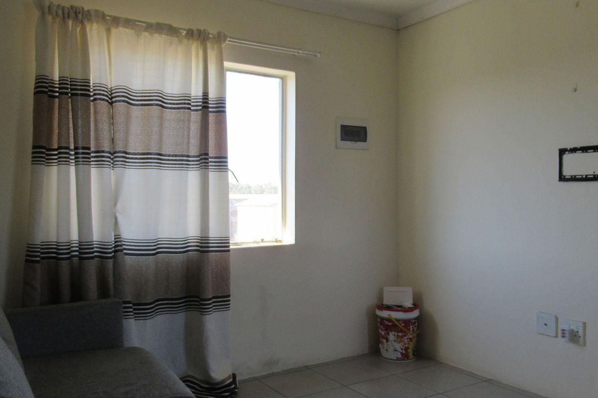 A simple living area featuring tiled flooring, a wall-mounted television bracket, and an electrical distribution board, offering a functional space for customization.