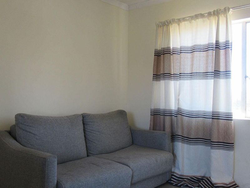 A simple living room area featuring a window with a curtain rail, providing natural light to the space.