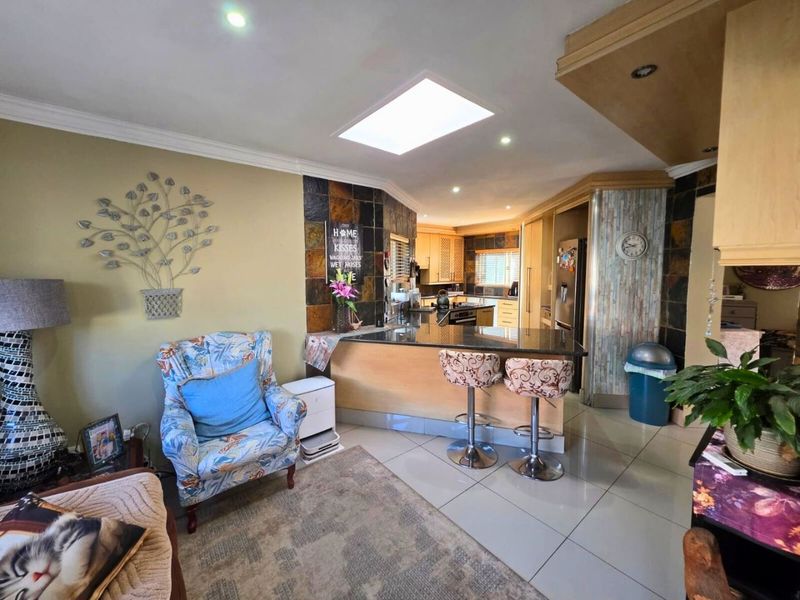 Open plan kitchen and living area featuring a central breakfast bar, stone wall accents, tiled flooring, and a skylight providing natural light.