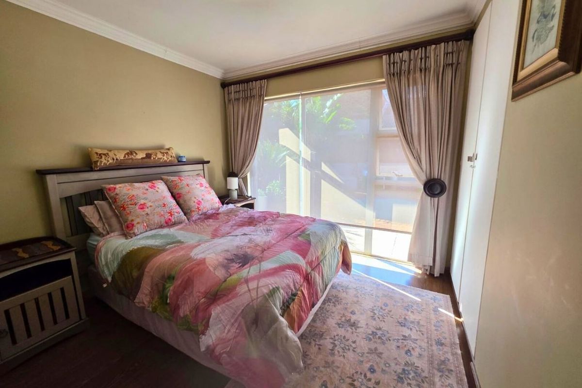 A cozy bedroom featuring built-in cupboards, wood-look flooring, and a sliding glass door that provides natural light and access to the exterior.
