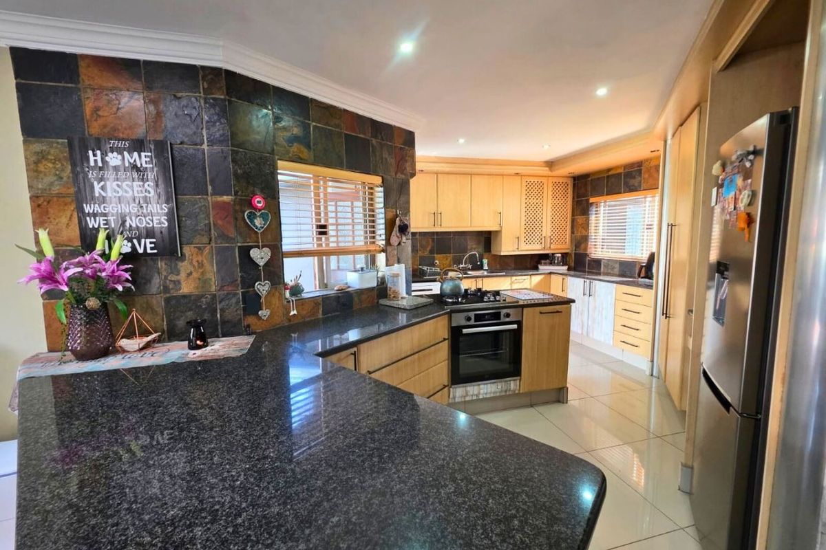 Spacious kitchen featuring granite countertops, timber cabinetry, a built-in oven with gas hob, and distinctive slate tile splashbacks.