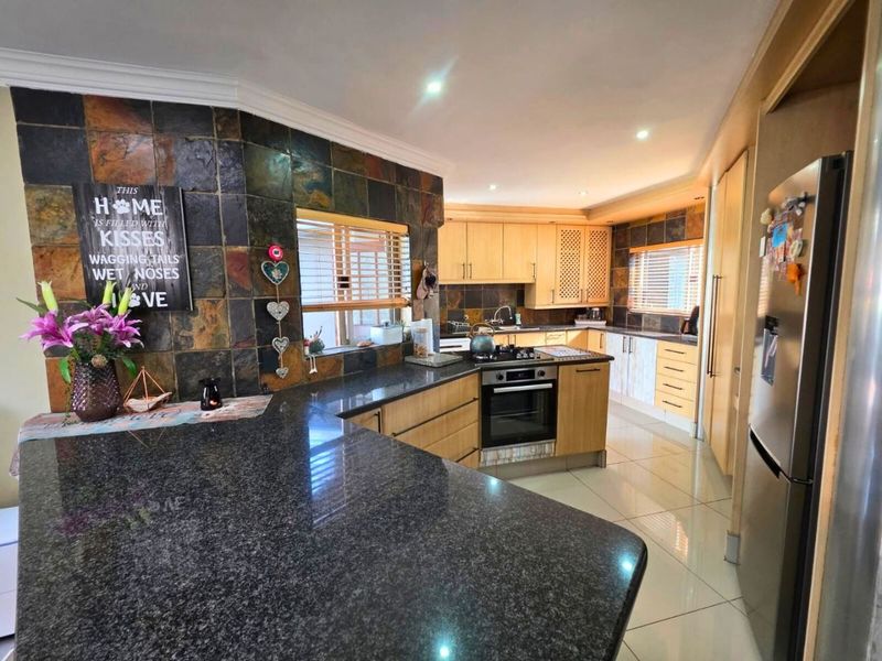 Spacious kitchen featuring granite countertops, timber cabinetry, a built-in oven with gas hob, and distinctive slate tile splashbacks.