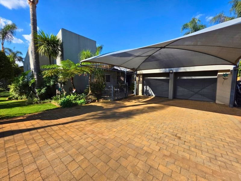 Front exterior view featuring a paved driveway, double garage with sectional doors, and a large shade sail structure set within a landscaped garden.