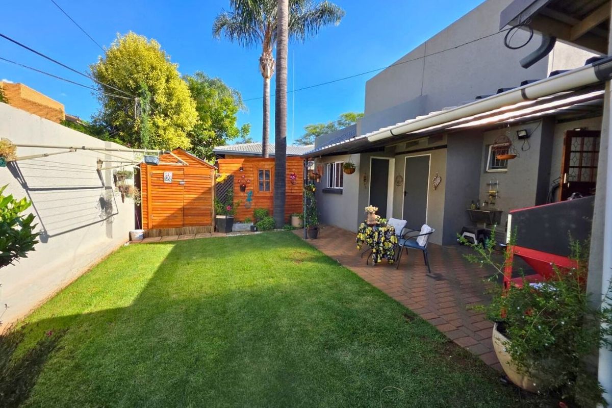 A well-maintained rear garden featuring a paved patio area, a neat lawn, and a wooden storage shed, providing a functional outdoor living space.