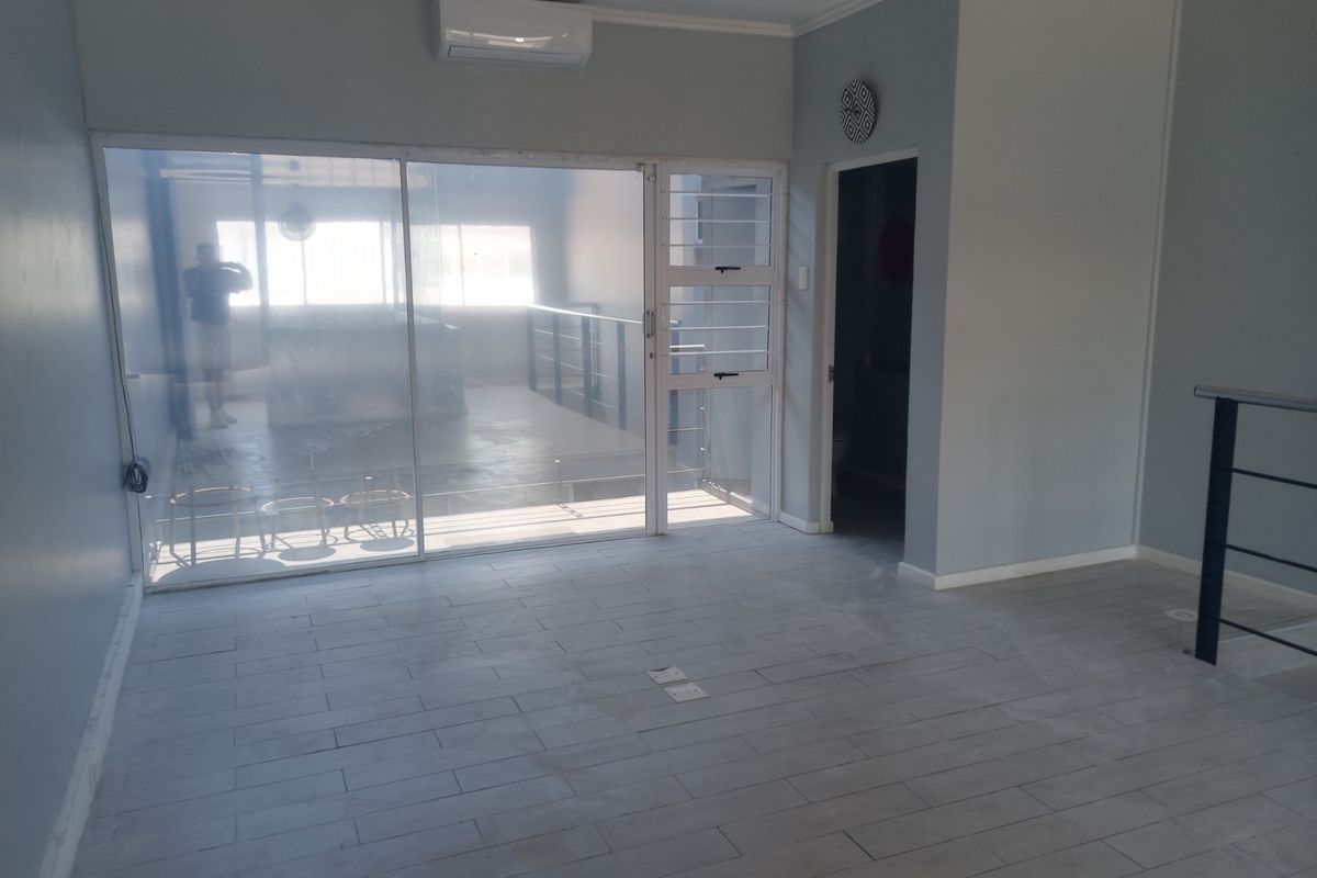 An empty, well-maintained living area featuring tiled flooring, a split-system air conditioner, and a large sliding glass door leading to an adjacent space.