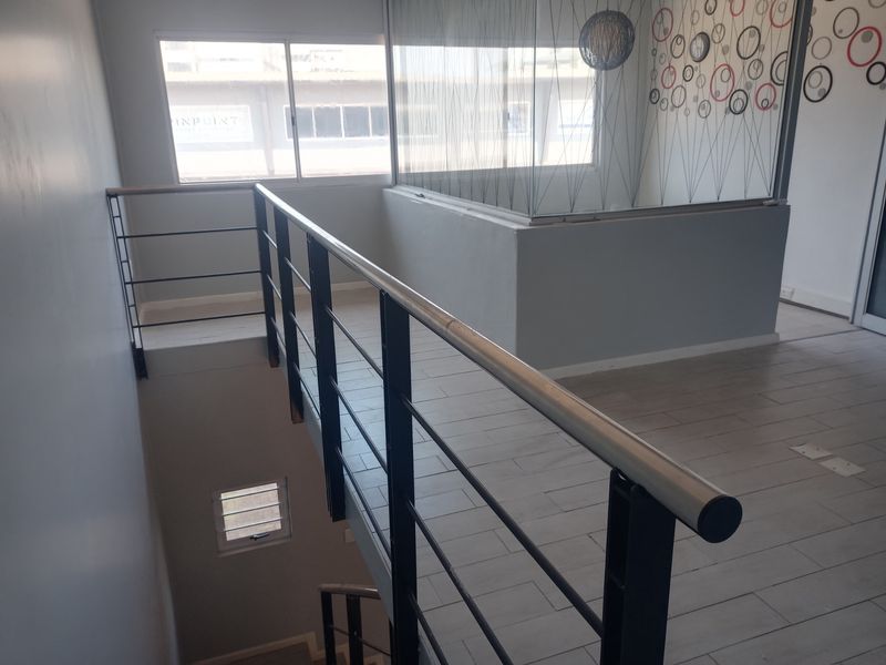 A bright, modern commercial hallway featuring tiled flooring, a sleek metal balustrade, and a glass partition overlooking the staircase area.