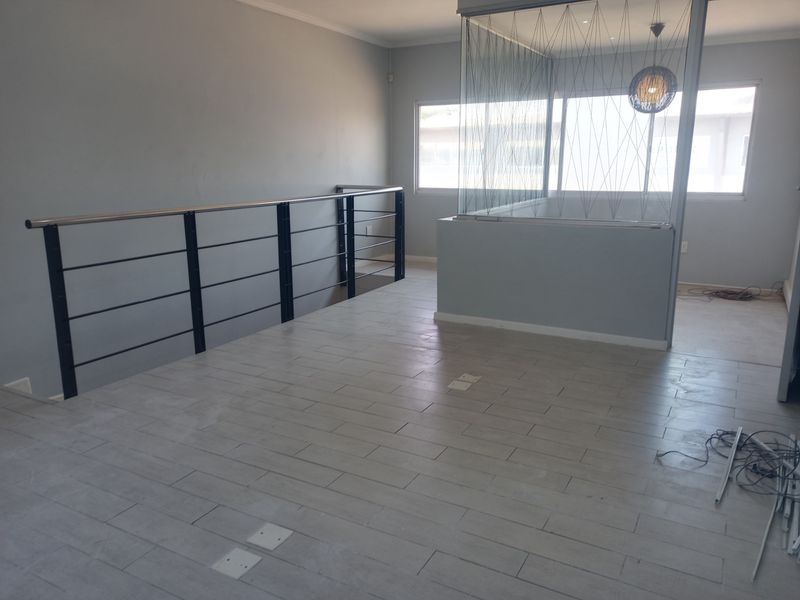 An open-plan office space featuring modern tiled flooring, a sleek metal balustrade, and a glass-partitioned area, offering a clean and versatile commercial layout.