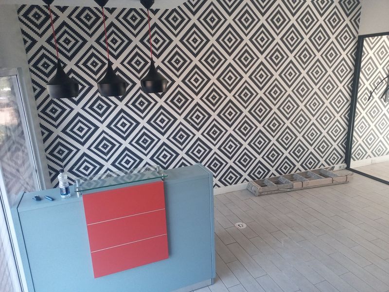 A commercial reception area featuring a modern built-in desk, geometric patterned feature wall, and contemporary pendant lighting.