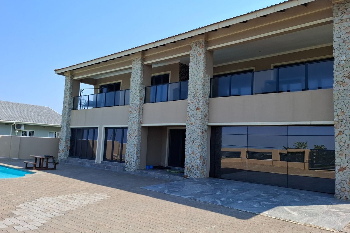 A modern two-story rear elevation featuring stone-clad pillars, glass balustrades, a paved patio area, and a swimming pool.
