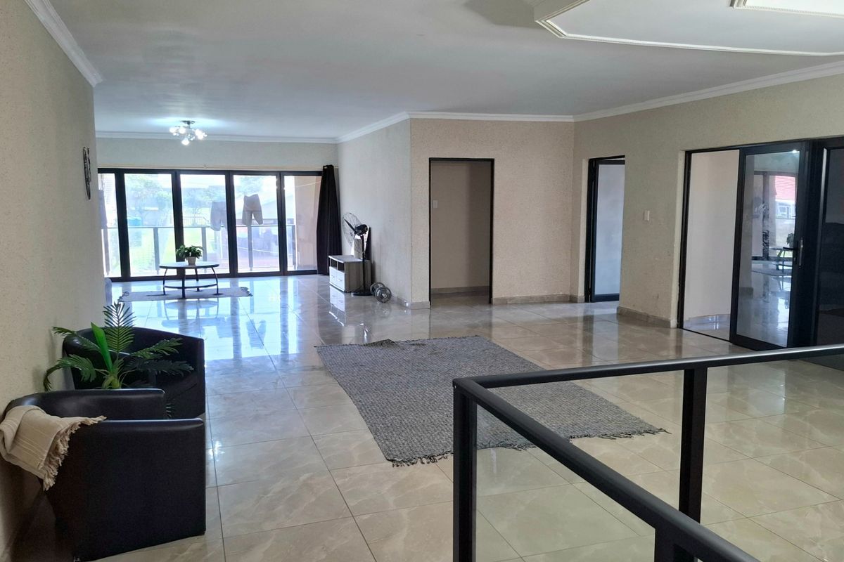 Spacious open-plan living area featuring large format floor tiles, modern glass balustrades, and expansive sliding doors leading to an outdoor balcony.