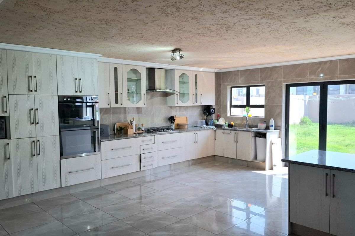 Spacious kitchen featuring light-toned cabinetry, granite countertops, built-in oven, gas hob, and direct access to the garden through glass sliding doors.