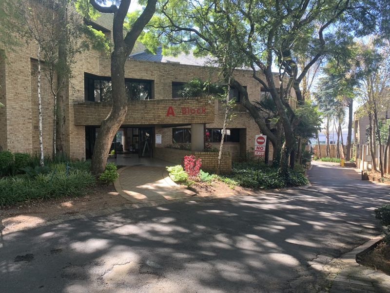 Front elevation of A Block commercial building featuring a brick facade, covered entrance, and mature landscaped surroundings with a paved driveway.