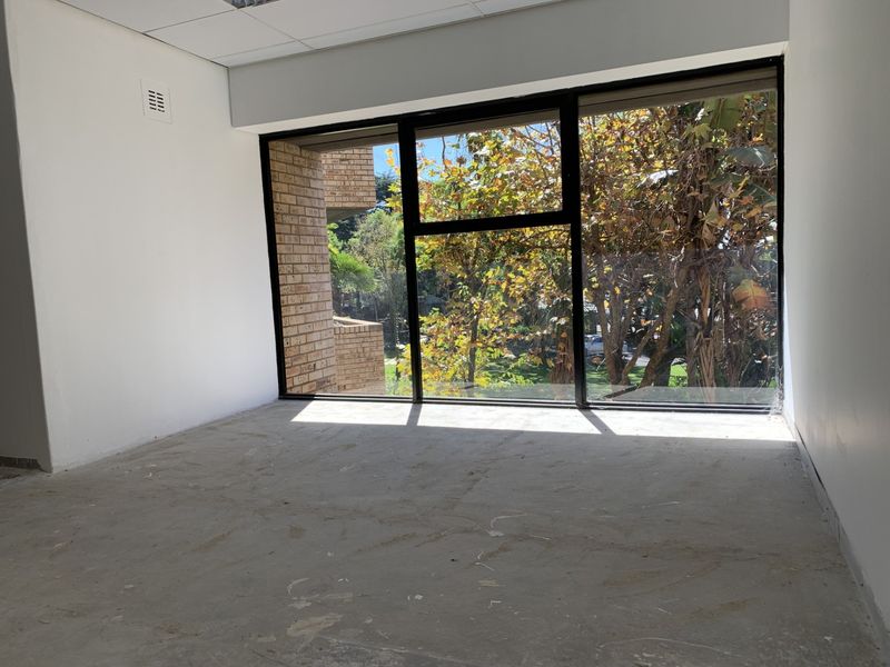 An empty office space featuring a large window with natural light and views, currently awaiting final flooring installation.