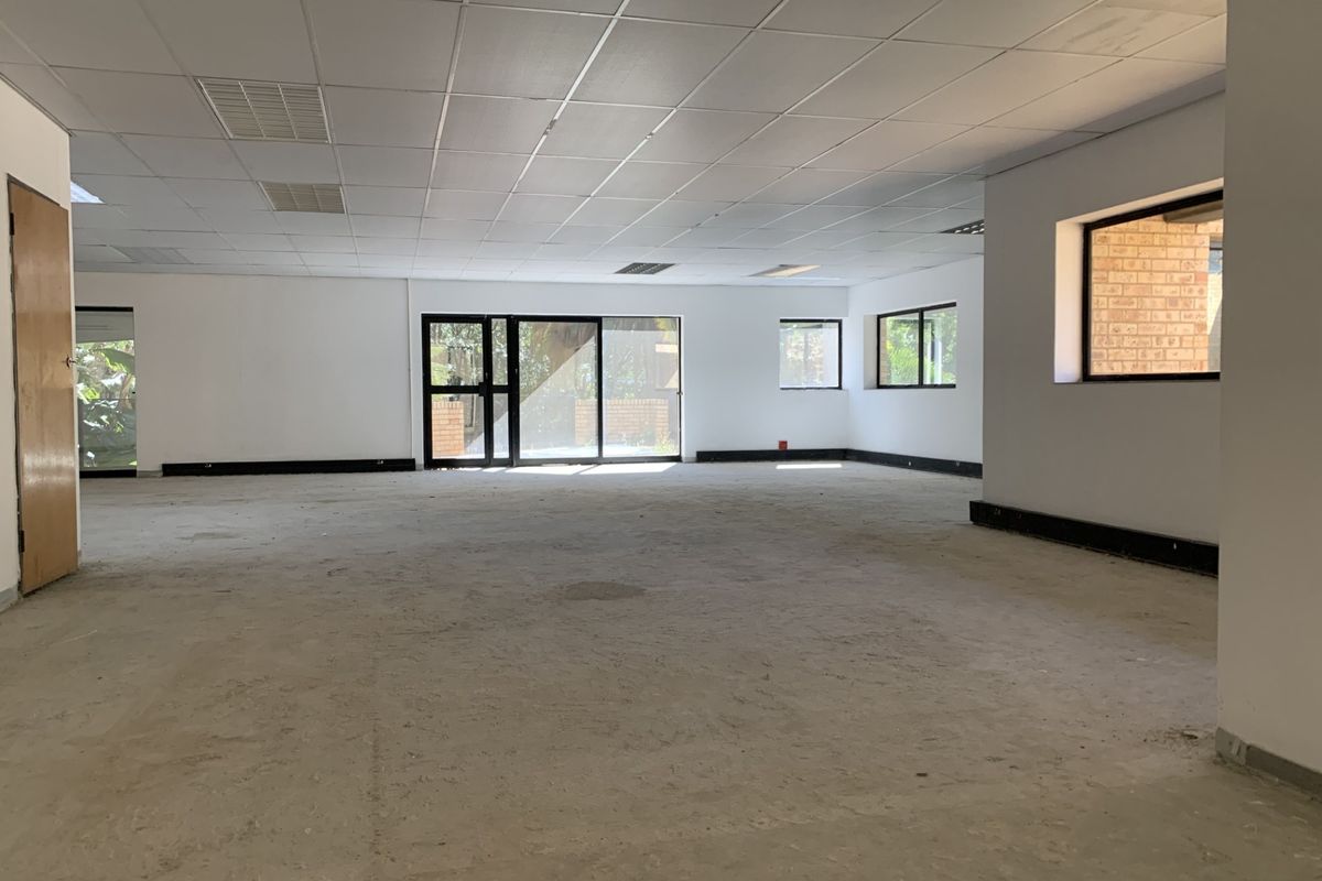 A spacious, vacant open-plan commercial office area featuring a suspended ceiling, recessed lighting, and large windows providing ample natural light.