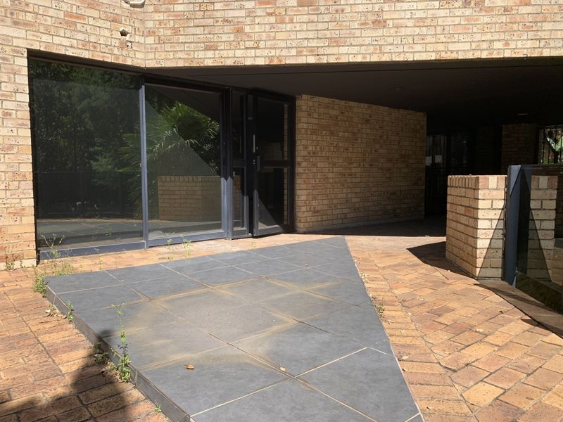 Rear exterior view of a commercial property featuring a face brick facade, paved patio area, and large sliding glass doors.