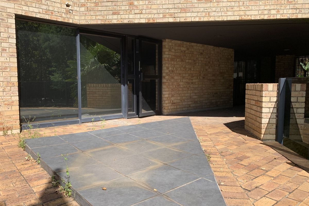 Rear exterior view of a commercial property featuring a face brick facade, paved patio area, and large sliding glass doors.