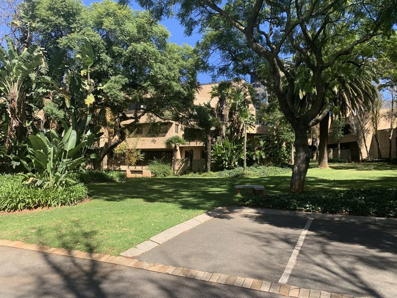 A view of the commercial property's rear exterior, featuring a well-maintained garden, mature trees, and paved parking area.