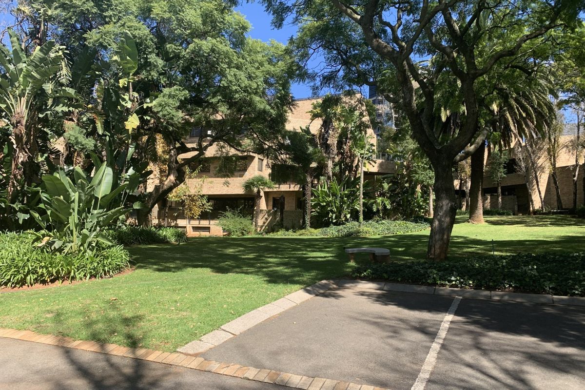 A view of the commercial property's rear exterior, featuring a well-maintained garden, mature trees, and paved parking area.
