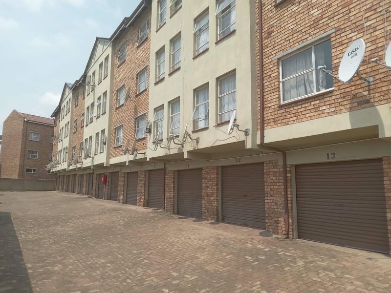 Exterior view of an apartment complex featuring a paved driveway and a row of individual roller shutter garage doors.