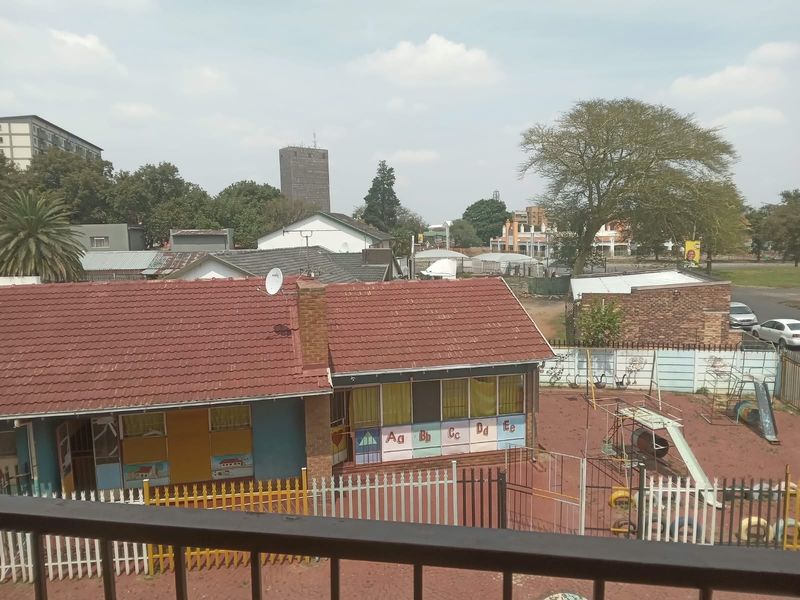 An elevated view overlooking a neighbouring property with a tiled roof, brick chimney, and a fenced outdoor play area.