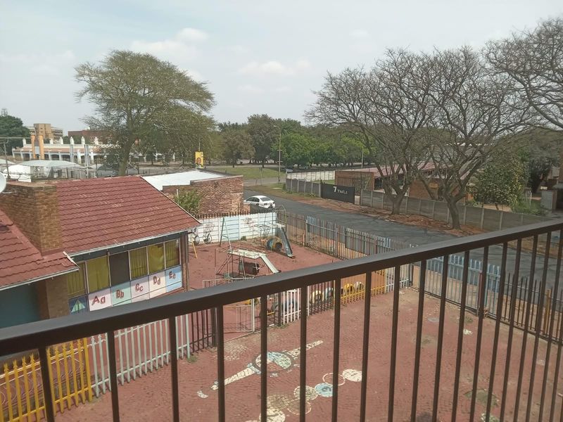 An elevated view overlooking a paved courtyard area with perimeter fencing and surrounding neighborhood infrastructure.