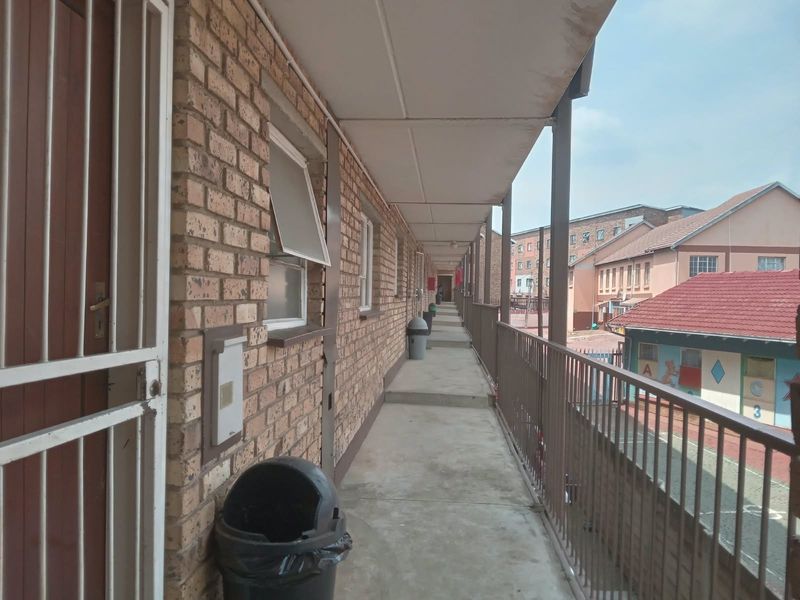 An exterior walkway or balcony area featuring brick walls, metal security gates, and a metal balustrade overlooking the complex grounds.
