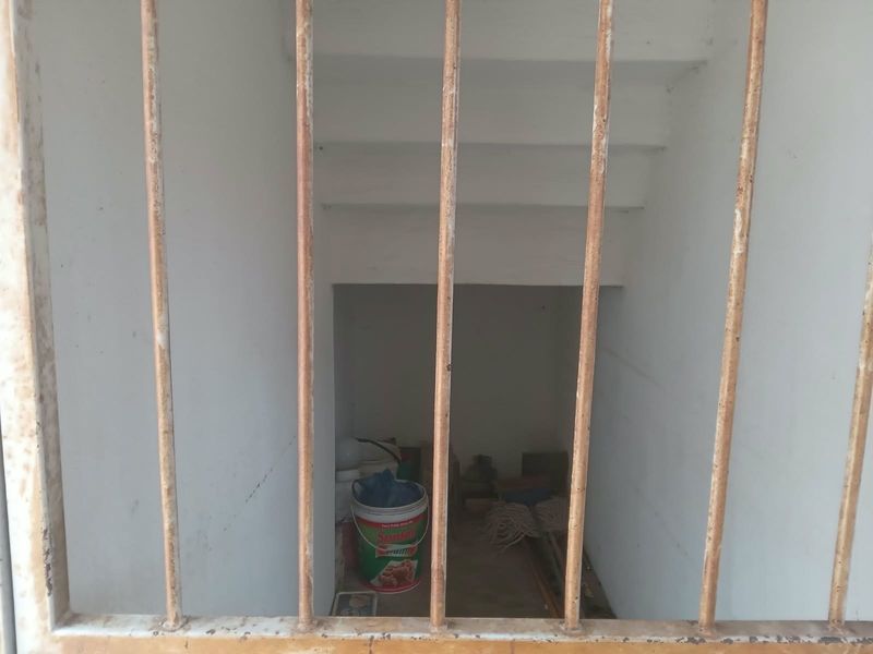 A small, enclosed utility or storage area accessed via a staircase, secured by rusted metal bars.