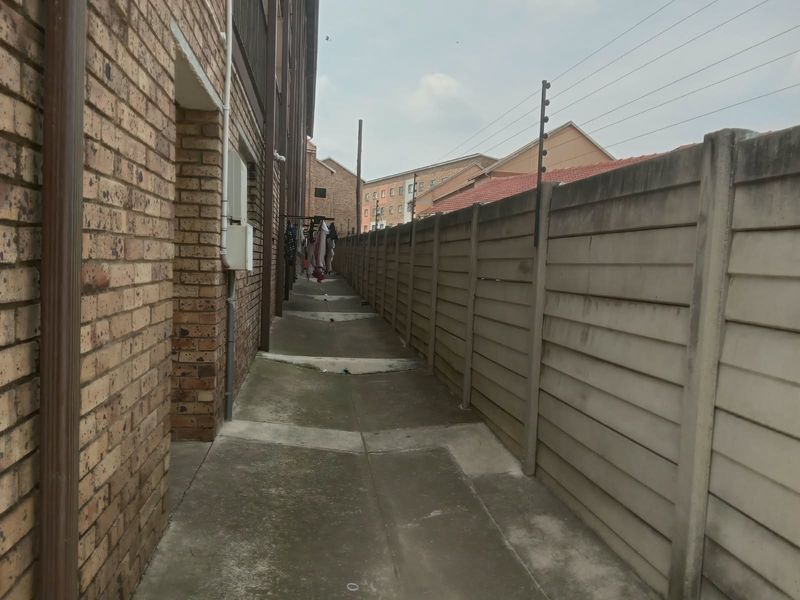 A narrow exterior side passage featuring face brick walling, concrete paving, and a precast boundary wall equipped with electric fencing.