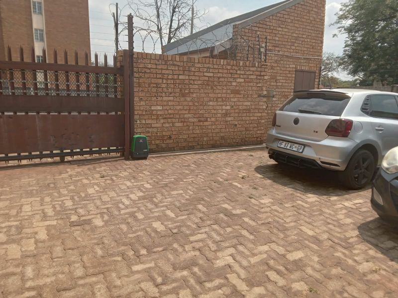 Front exterior view of the property featuring a paved driveway, secure brick boundary wall with electric fencing, and a sliding gate with motor.