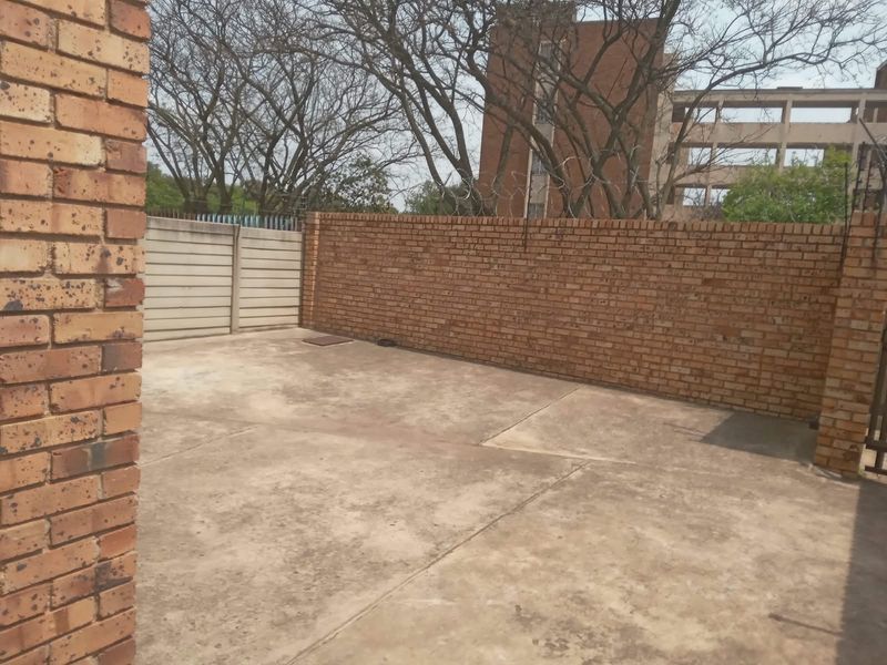 A private rear courtyard area featuring concrete paving and high brick boundary walls with security razor wire.
