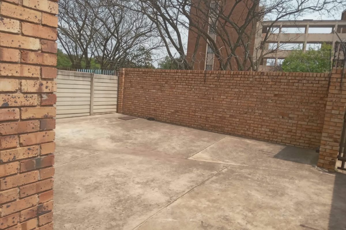 A private rear courtyard area featuring concrete paving and high brick boundary walls with security razor wire.