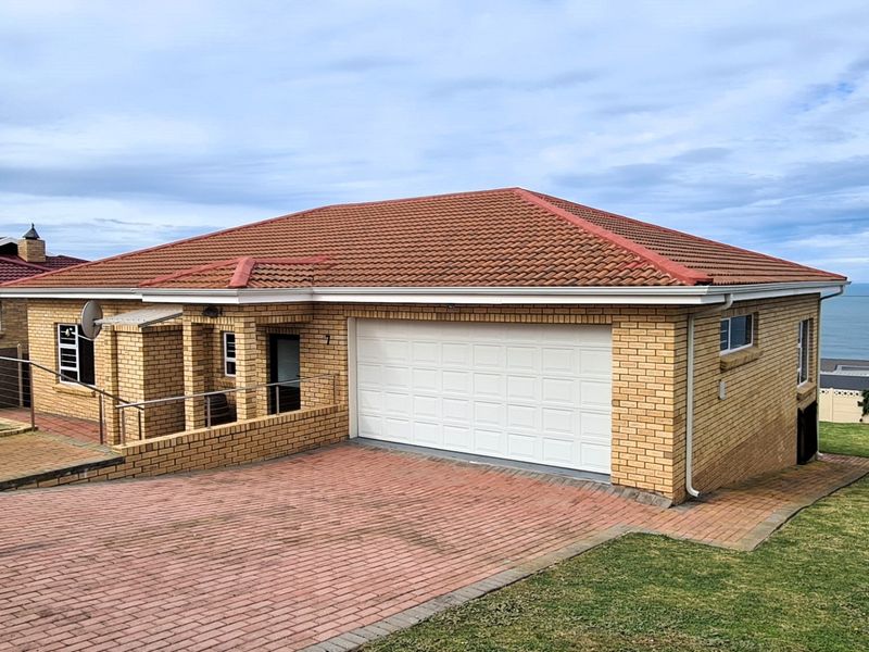 A well-maintained single-story brick house featuring a tiled roof, a double garage, and a paved driveway, situated with a view of the ocean.