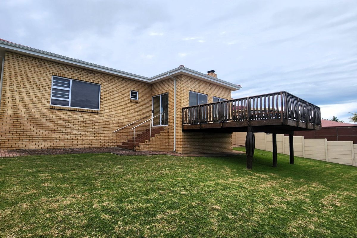 Rear view of a brick house featuring a raised timber deck, sliding glass door access, and a spacious backyard with a boundary wall.