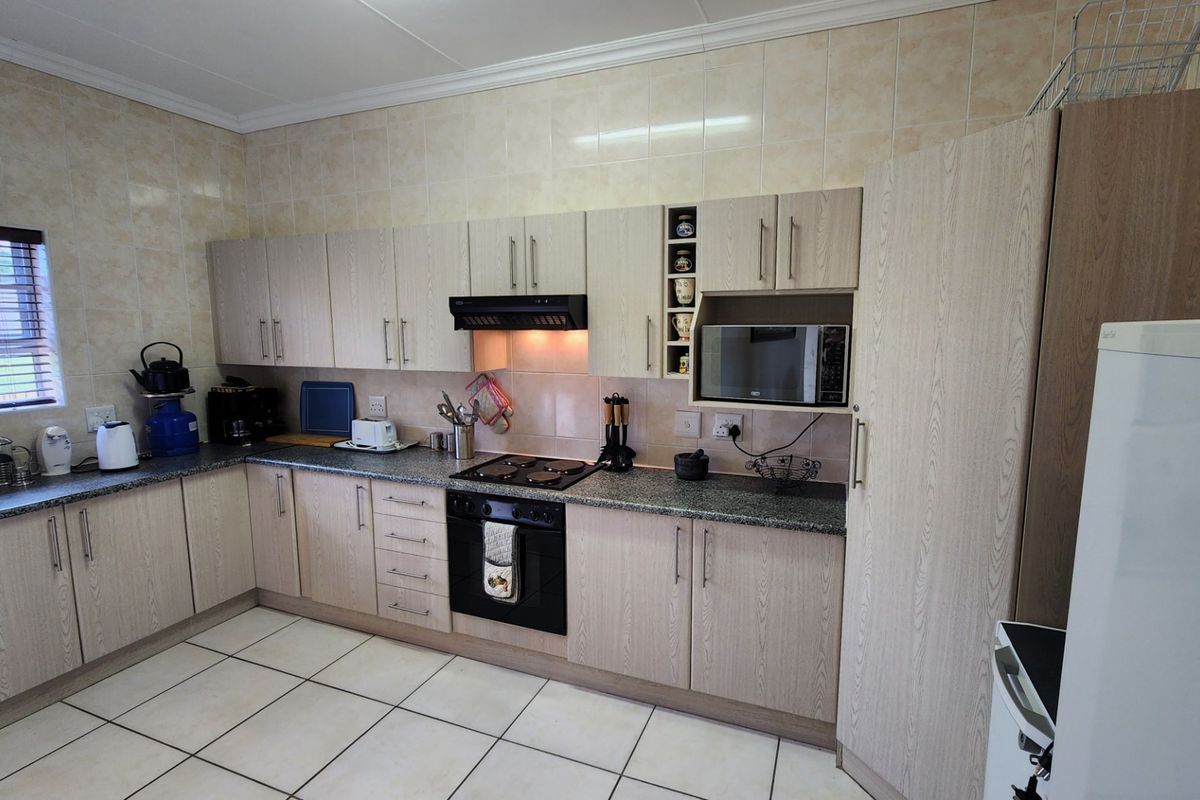 Functional kitchen featuring light wood-grain cabinetry, granite countertops, ceramic tile backsplash, and integrated appliances including an oven, hob, and microwave.
