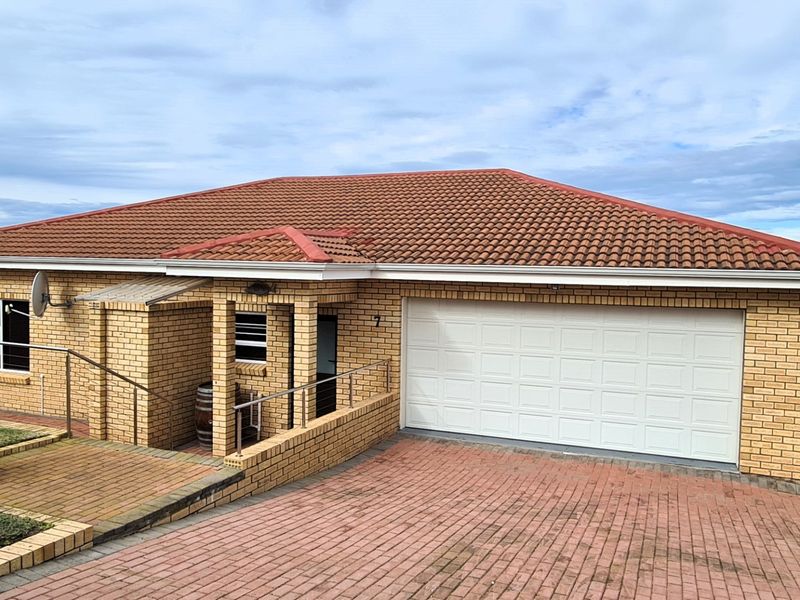 A well-maintained face brick house featuring a tiled roof, paved driveway, and an integrated double garage with a paved entrance area.