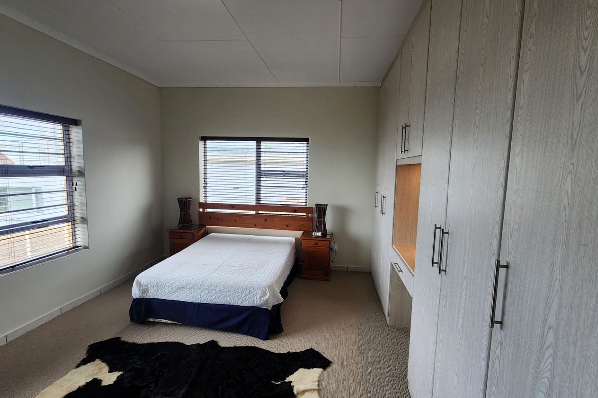 Spacious bedroom featuring extensive built-in cupboards with an integrated vanity, neutral carpeting, and large windows with venetian blinds.