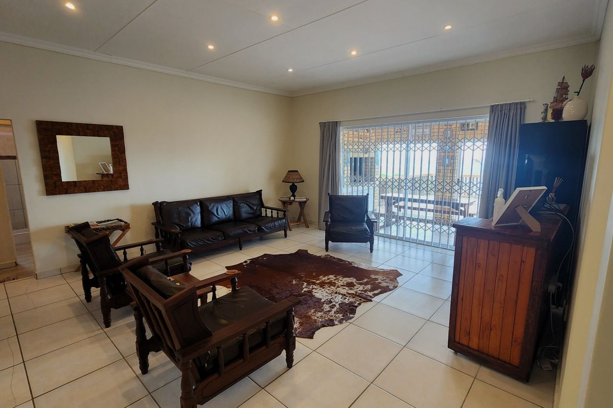 Spacious living room featuring tiled flooring, recessed downlighting, and a sliding glass door with security gate leading to the outdoor area.