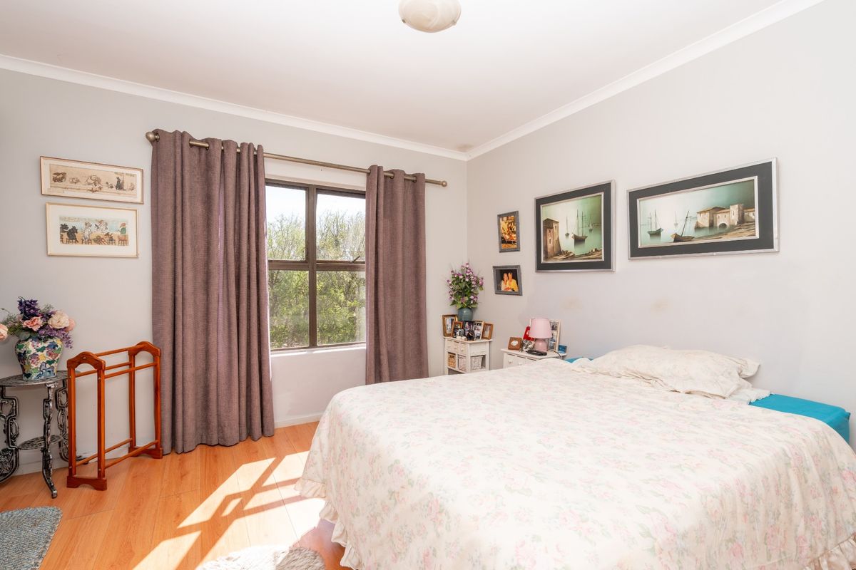 A well-lit bedroom featuring laminate flooring, neutral wall finishes, and a window with curtain tracks.