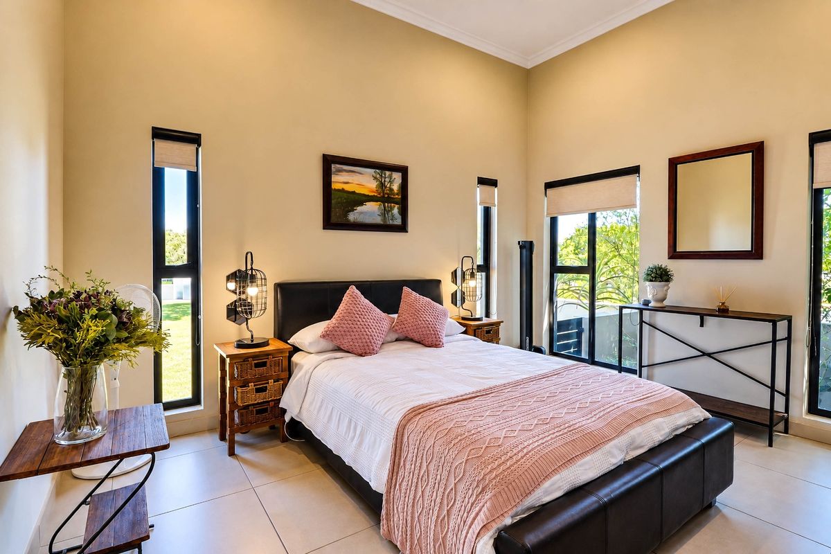 A bright and spacious bedroom featuring high ceilings, large windows with roller blinds, and neutral tiled flooring, offering a comfortable and well-maintained living space.