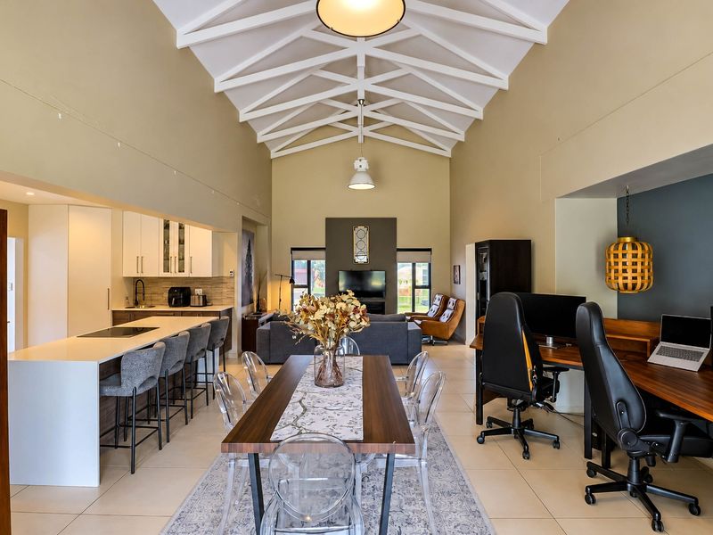 Spacious open-plan living area featuring a high vaulted ceiling with exposed trusses, a modern kitchen with island, and integrated workspace.
